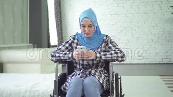美丽的年轻女子戴着头巾残疾轮椅使用电话看着摄像机视频的预览图
