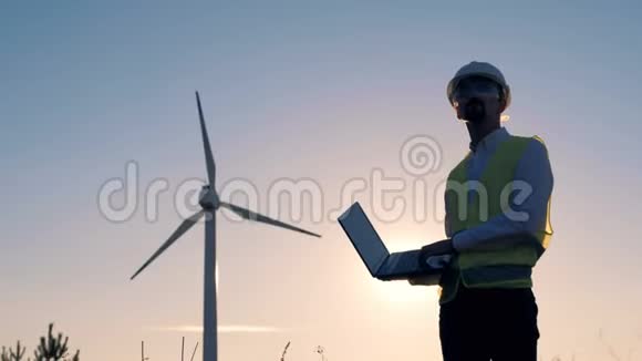男工程师手里拿着一台笔记本电脑打字并检查电动风车可再生电能绿色能源概念视频的预览图