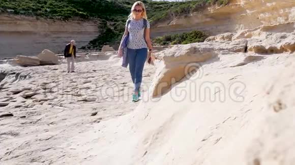 在一个风和日丽的日子里两个游客沿着海洋的岩石海岸在巨大的棕色石头粘土中散步然后视频的预览图