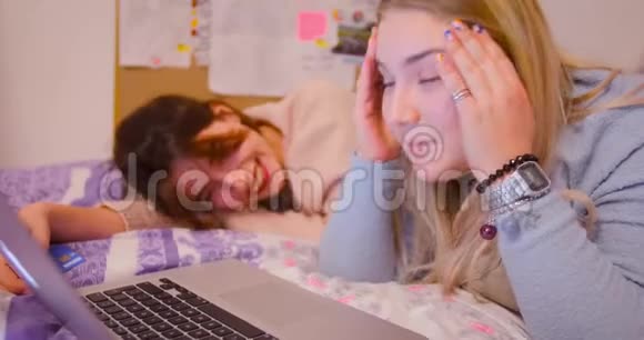 两个可爱的女孩深褐色的红唇和丰满的金发躺在笔记本电脑前的床上笑着说视频的预览图