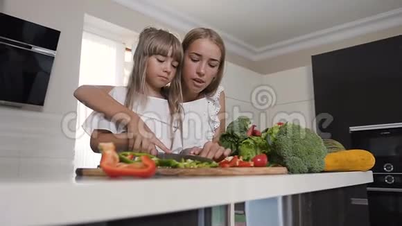 两个穿白色连衣裙的女孩正在家厨房里切蔬菜两个迷人的女孩在准备沙拉吸引力视频的预览图