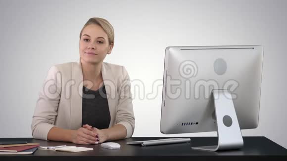 开朗的女商人坐在办公室的桌子上在渐变背景下看着相机视频的预览图