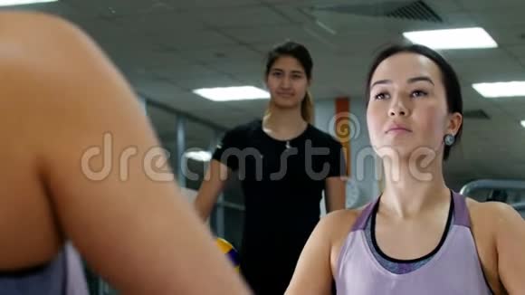 一个年轻的女人用哑铃抽她的手肌肉照镜子在教练的监视下视频的预览图