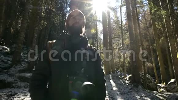 一位留着胡子的严肃摄影师的肖像他背着背包和一架照相机站在针叶林中视频的预览图