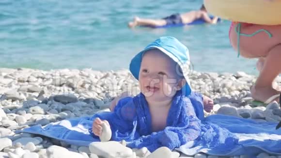 可爱的小男孩带着帽子坐在海滩上微笑视频的预览图