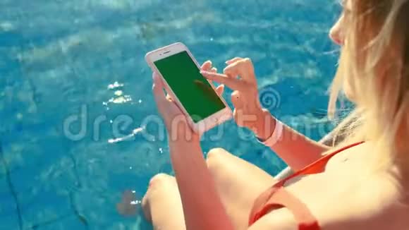 女孩使用垂直手机绿色屏幕同时放松附近的游泳池手拿智能手机铬钥匙视频的预览图