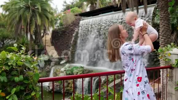 一位年轻的母亲带着一个孩子旅行在瀑布附近玩耍和拥抱她的儿子亲吻宝宝的脸颊视频的预览图