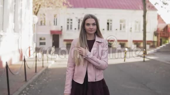 穿着粉色夹克的漂亮女孩走在城市里慢悠悠地对着镜头微笑视频的预览图
