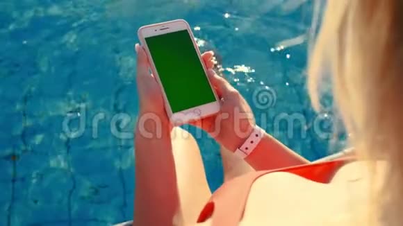 女孩使用垂直手机绿色屏幕同时放松附近的游泳池手拿智能手机铬钥匙视频的预览图