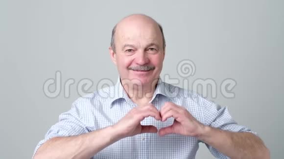 老人用手指微笑着看着相机做着心形的爱标志视频的预览图