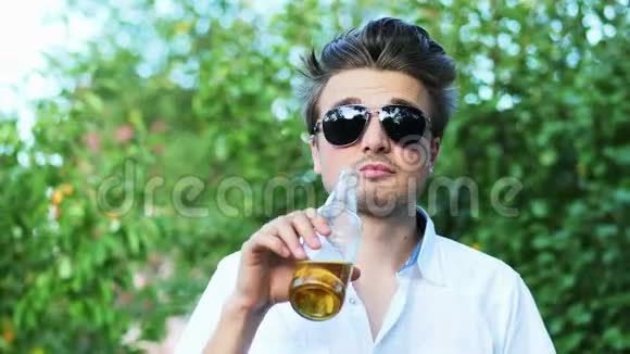 太阳眼镜中快乐男人的特写镜头日落时在公园休息时喝啤酒视频的预览图