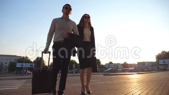 商人和他的女同事走在城市街道上用轮子滚动手提箱商业男女视频的预览图