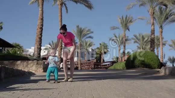 母亲带着孩子走在棕榈树附近的街道上视频的预览图