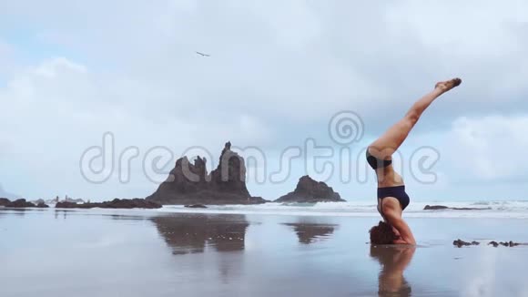 站在她头上的女孩在海滩上做瑜伽视频的预览图