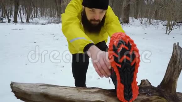 冬季森林跑步前伸展双腿的运动员视频的预览图