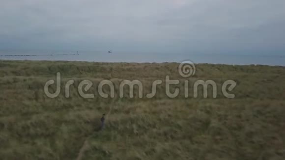 旅行穿过一个游客的绿色田野带着一个袋子走到海滩从空中拍摄无人机的视频视频的预览图