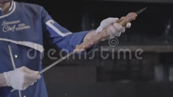 穿着蓝色厨师制服的熟练男子将肉串在扦子上在现代餐厅形成卢拉串大型烤炉视频的预览图