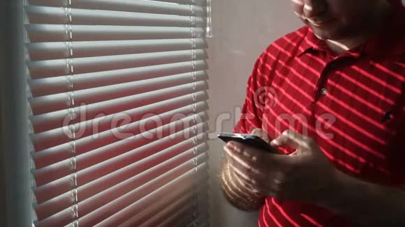 一名男子站在酒店房间靠窗的位置使用智能手机视频的预览图