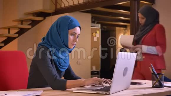 两位阿拉伯年轻女性办公室工作人员在头巾上的特写肖像讨论图表上的数据年轻视频的预览图