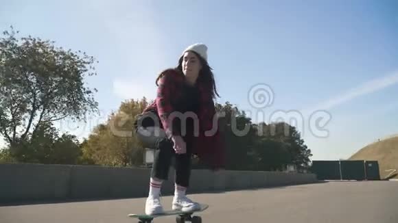 穿着白色帽子和格子衬衫的滑板女孩在户外玩滑板嬉皮士女孩在公园玩滑板视频的预览图