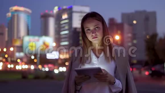 有魅力的女孩拿着平板电脑看着相机微笑着对着夜路视频的预览图