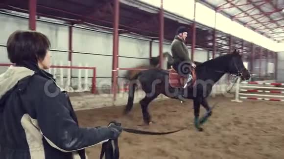 在特殊的机库里一个年轻的残疾人学会骑马与密切的监督老师嬉皮士治疗人类视频的预览图