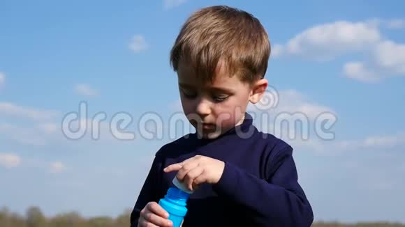 小男孩吹泡泡快乐的孩子在春天在公园里吹肥皂泡慢动作视频的预览图
