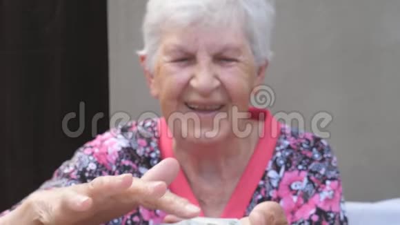 快乐的祖母手里拿着一捆钱把外币撒在桌子上老笑的画像视频的预览图