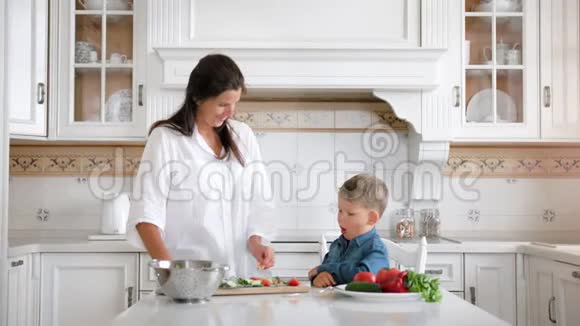 爱笑的女人一边做饭一边用新鲜的有机蔬菜喂小可爱的男孩视频的预览图