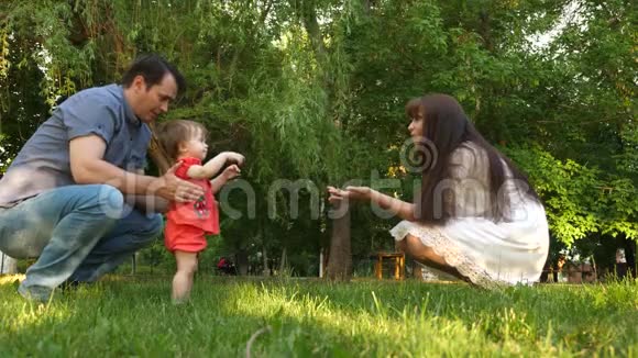 爸爸和妈妈学习在绿草地上公园里散步小女儿妈妈亲吻女儿的脸颊和爸爸一起笑视频的预览图