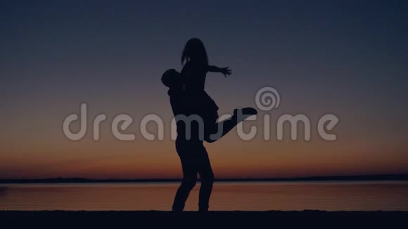 一对浪漫的情侣在夕阳下亲吻一个男人抱着女人纺纱的剪影视频的预览图