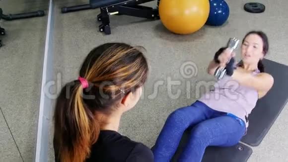 培训一位年轻女子拿着哑铃和教练一起抽着腹肌视频的预览图