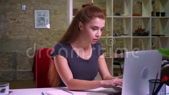 疲惫可爱的姜白女孩坐在办公室看着她的笔记本电脑放松许多工作要做办公室氛围视频的预览图