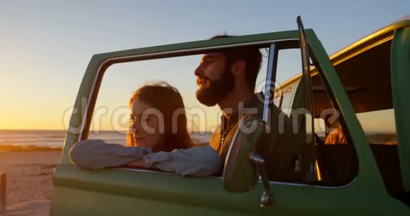 日落时分一对年轻夫妇站在4k海滩的货车窗前视频的预览图