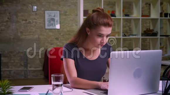 漂亮的红头发女孩坐在电脑上工作然后高兴地看着相机愉快的微笑和自然视频的预览图