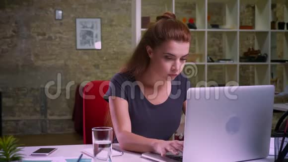 集中姜黄白种人的女人在笔记本电脑上打字一边平静地坐在她的现代生活中一边晃晃悠悠视频的预览图
