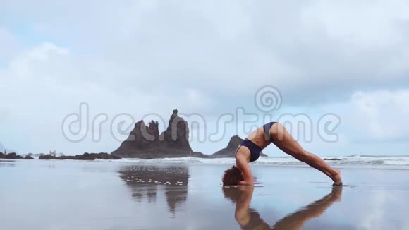 日落时分的女子瑜伽练习勇女慢动作在美丽的海滩上倒立做瑜伽运动视频的预览图