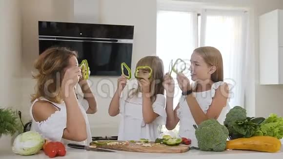 年轻的母亲和美丽的两个女儿一起在家厨房准备沙拉他们在玩胡椒片视频的预览图