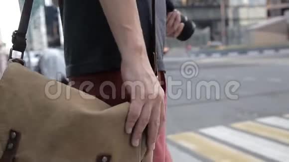 一个人在一个行人过路处穿过马路手里拿着一个照相机放在他的肩包上在一个视频的预览图