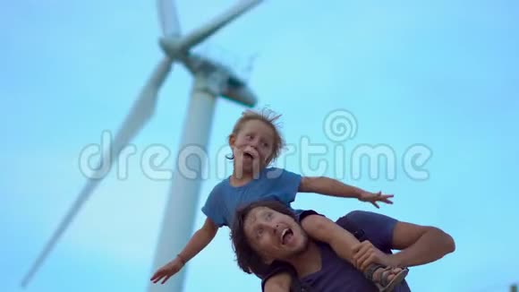 父子俩玩得很开心站在海边山顶的风力发电机下清洁能源概念视频的预览图