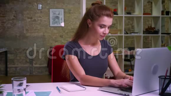 快乐的白种人工作的红发女看着笔记本电脑屏幕一边微笑一边高兴地拍手视频的预览图