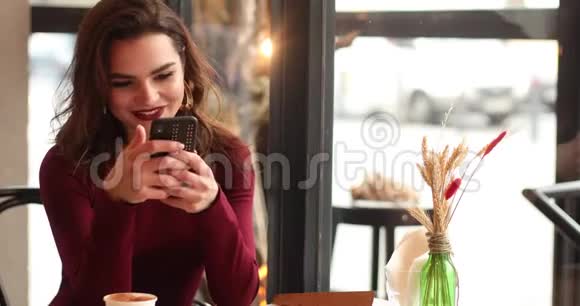 时尚的红色女士在咖啡馆里用手机视频的预览图