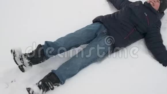小男孩躺在雪地里在冬天的森林里玩耍美丽的风景和雪杉树视频的预览图
