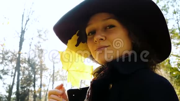 戴帽子的漂亮女人的肖像女孩在手中的特写镜头中旋转着一片黄色的枫叶视频的预览图