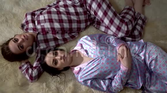 两个穿着睡衣的双胞胎姐妹躺在柔软的地毯上面对着对方进行着愉快的晚间谈话关系视频的预览图