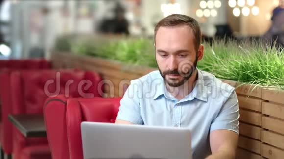 自信的白人年轻人在舒适的咖啡店或咖啡馆里使用笔记本电脑视频的预览图