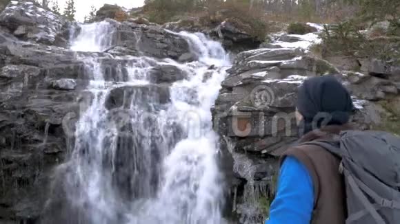 旅行者带着背包在美丽的瀑布前休息他用铁杯喝热茶视频的预览图