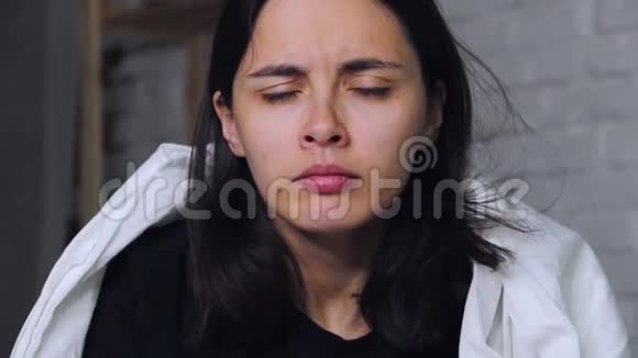一个年轻的女人坐在家里的床上病了用手帕吹鼻子视频的预览图