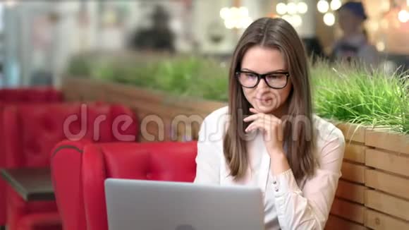 带着微笑的沉思的年轻女商人戴着眼镜使用笔记本电脑的画像视频的预览图