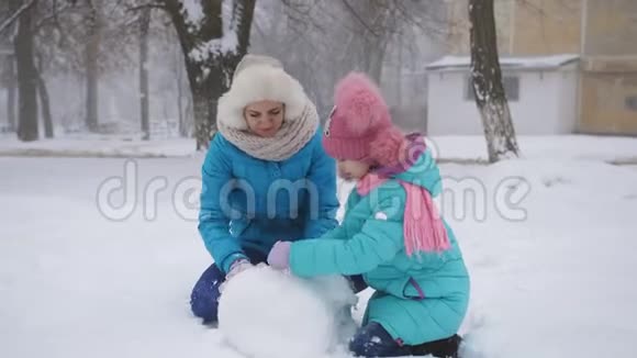 冬天的妈妈和小女儿在街上堆雪人视频的预览图